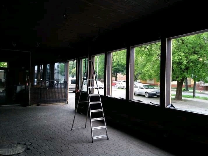 Wnętrze lokalu z odsłoniętymi ramami okiennymi, przygotowane do prac wykończeniowych, z rozstawioną drabiną aluminiową na tle ulicy z zaparkowanymi samochodami.