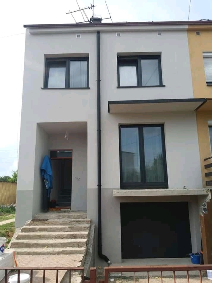 Dwukondygnacyjny budynek po odświeżeniu elewacji w odcieniach szarości, z widocznym wejściem, schodami i fragmentem posesji.