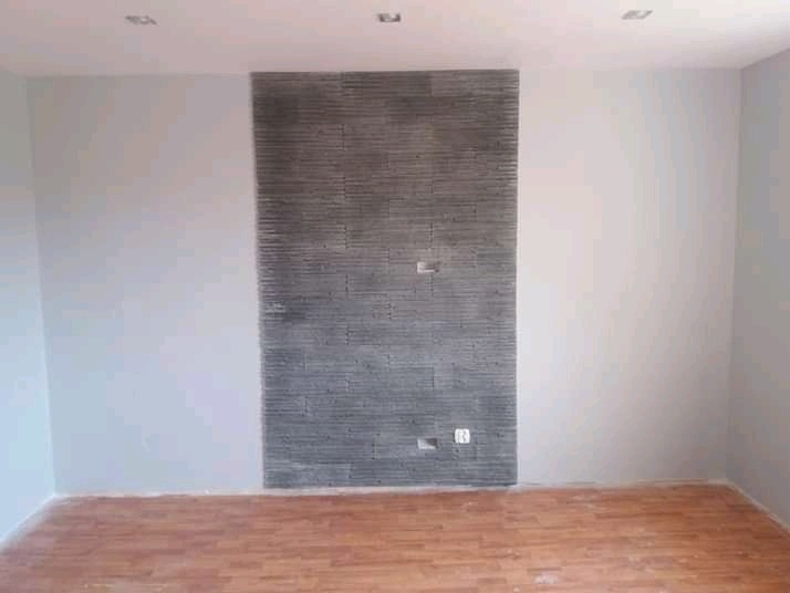 Świeżo pomalowane wnętrze z dekoracyjną ścianą imitującą kamień, widoczne gniazdko elektryczne i drewniana podłoga.