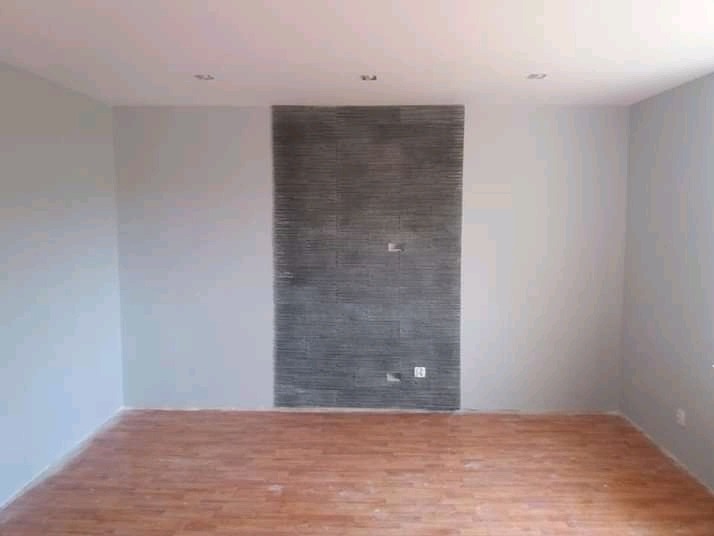 Pomalowane na szaro ściany pomieszczenia z dekoracyjną ścianą z efektem cegły, drewnopodobna podłoga, sufit z oświetleniem punktowym.