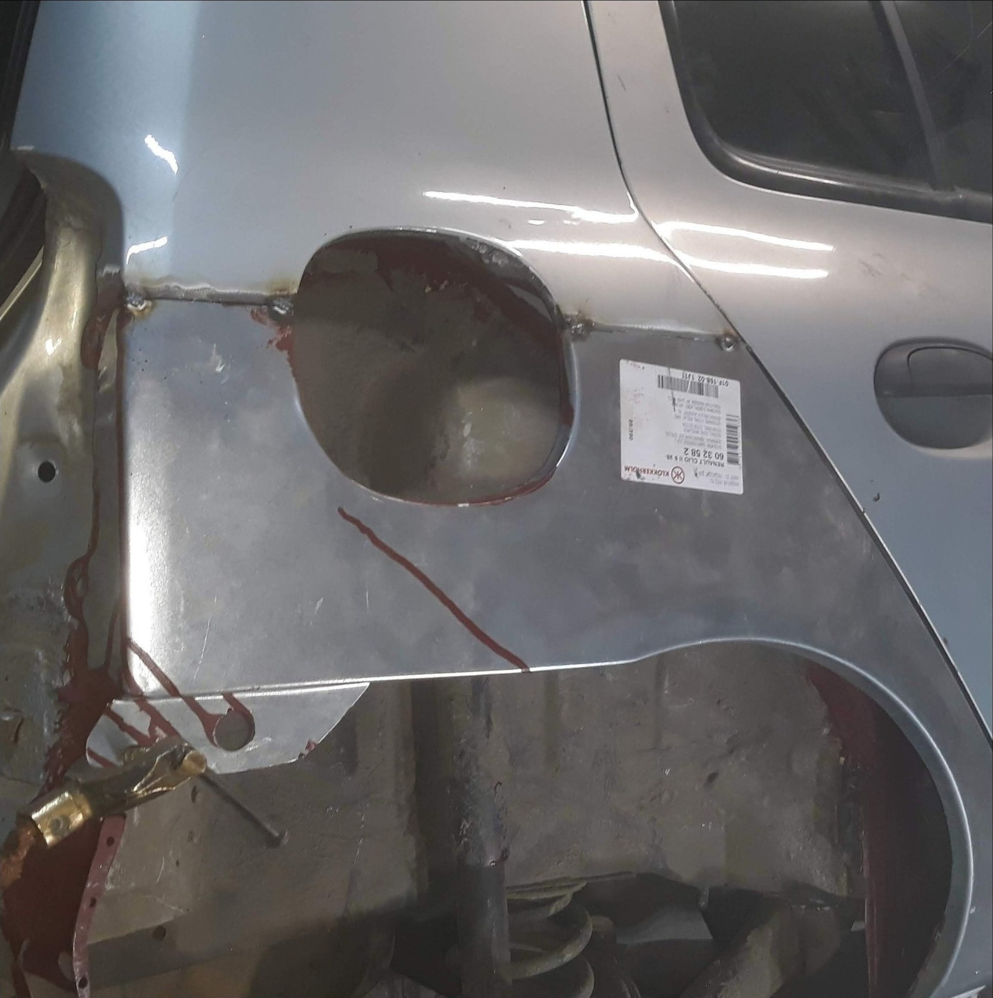 Naprawa karoserii samochodu: wspawana blacha w miejscu uszkodzenia, widoczne ślady spawania i resztki farby zabezpieczającej.