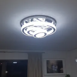 Nowoczesna, okrągła lampa sufitowa LED z kryształkami, zamontowana w salonie z widokiem na okno i rośliny doniczkowe.