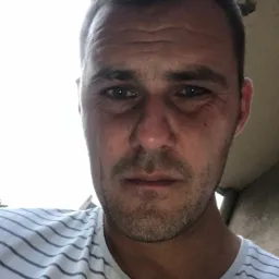 Portret dekarza w paski, z widocznymi zmarszczkami na czole i lekkim zarostem, wykonany w słoneczny dzień prawdopodobnie na dachu.