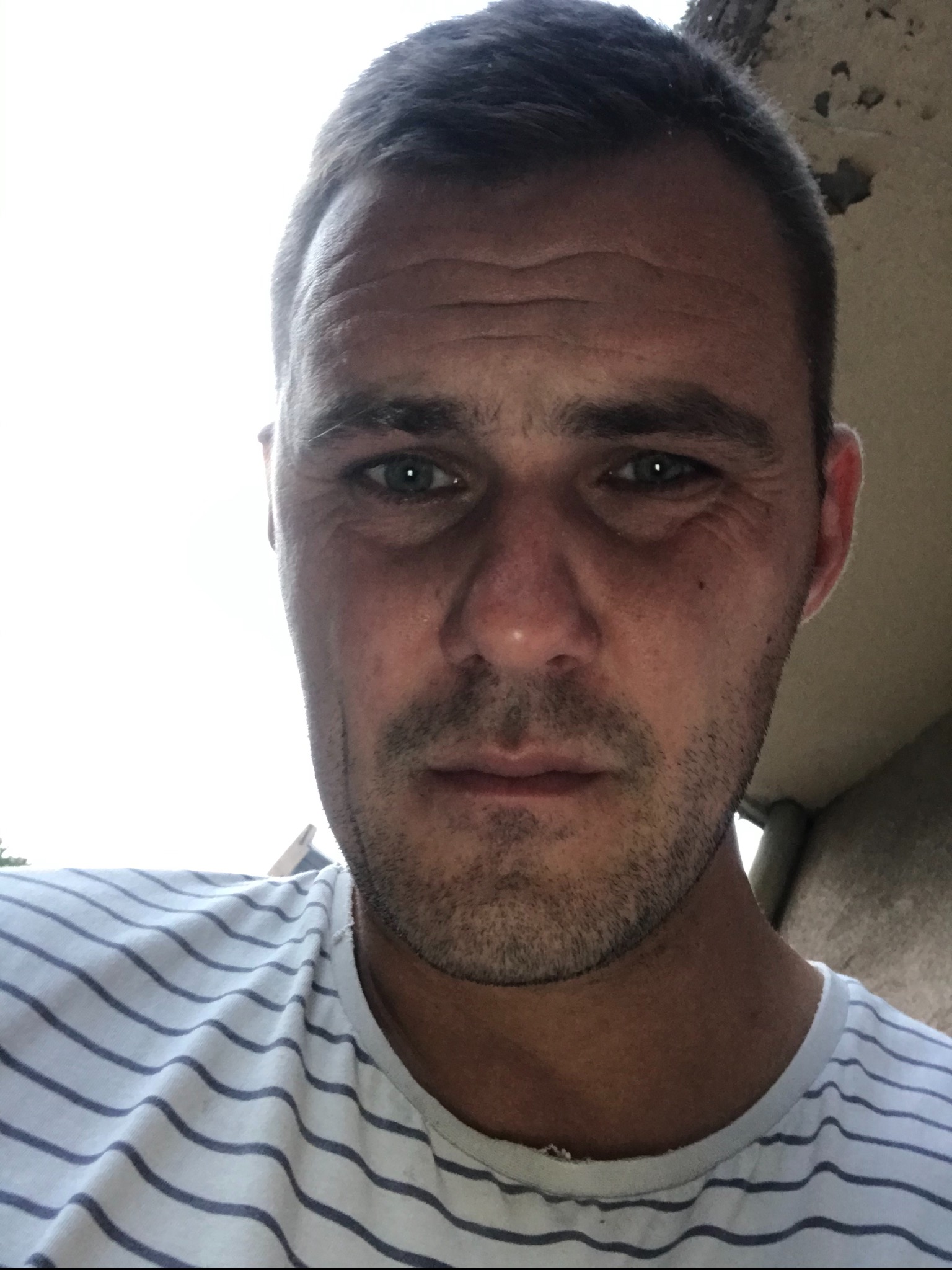 Portret dekarza w paski, z widocznymi zmarszczkami na czole i lekkim zarostem, wykonany w słoneczny dzień prawdopodobnie na dachu.