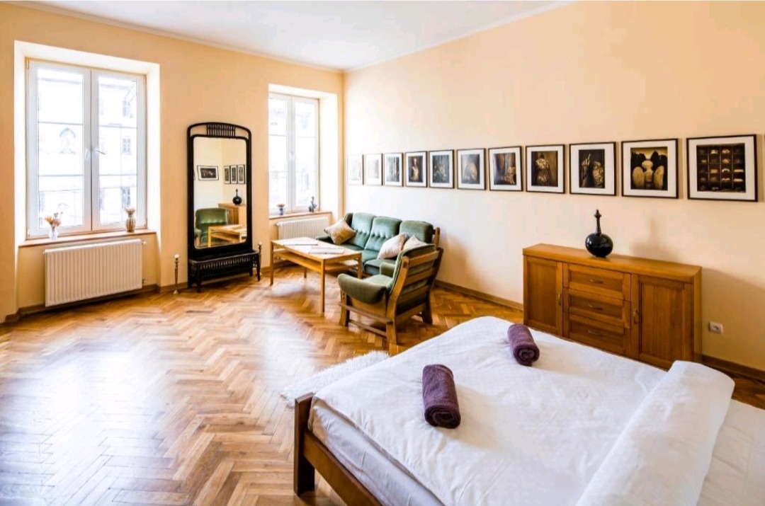 Jasne wnętrze pokoju z łóżkiem, zieloną sofą i drewnianą podłogą w jodełkę po odświeżeniu koloru ścian.