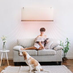 PHU AP Service Artur Zioło - Kobieta w kwiecistej sukience siedzi na szarej kanapie z tabletem, pod nowoczesnym panelem grzewczym, obok siedzi pies rasy beagle na wzorzystym dywanie, w tle biała ściana i grzejnik żeberkowy.