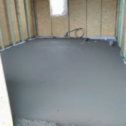 Wylewka jastrychowa na podłodze w surowym wnętrzu z drewnianą konstrukcją ścian i oknem zasłoniętym folią.