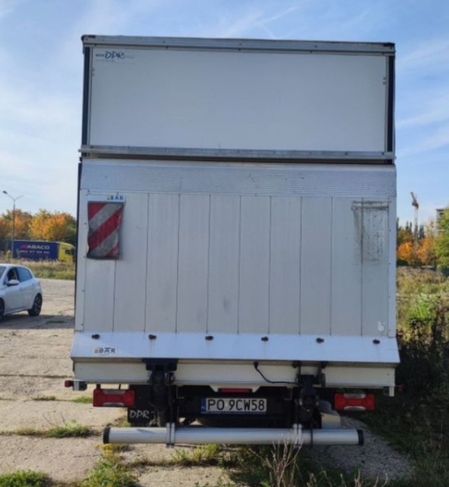 Tył białego busa z zabudową kontenerową, widoczny numer rejestracyjny PO 9CW58, oraz odblaskowa tablica ostrzegawcza.