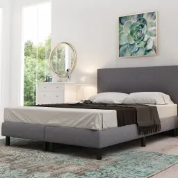 Szare łóżko tapicerowane z zagłówkiem i pościelą w jasnym pokoju z oknami i dekoracjami.