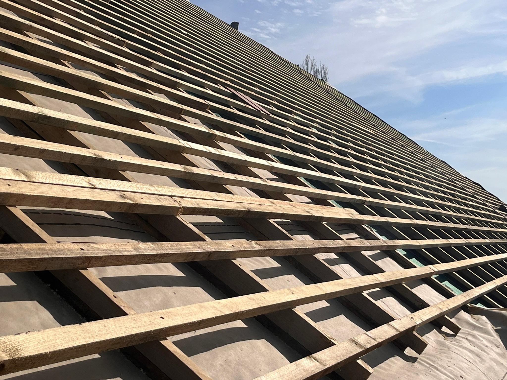 Widok z dołu na konstrukcję drewnianą dachu pokrytą membraną, przygotowaną pod dalsze prace dekarskie, na tle jasnego nieba.