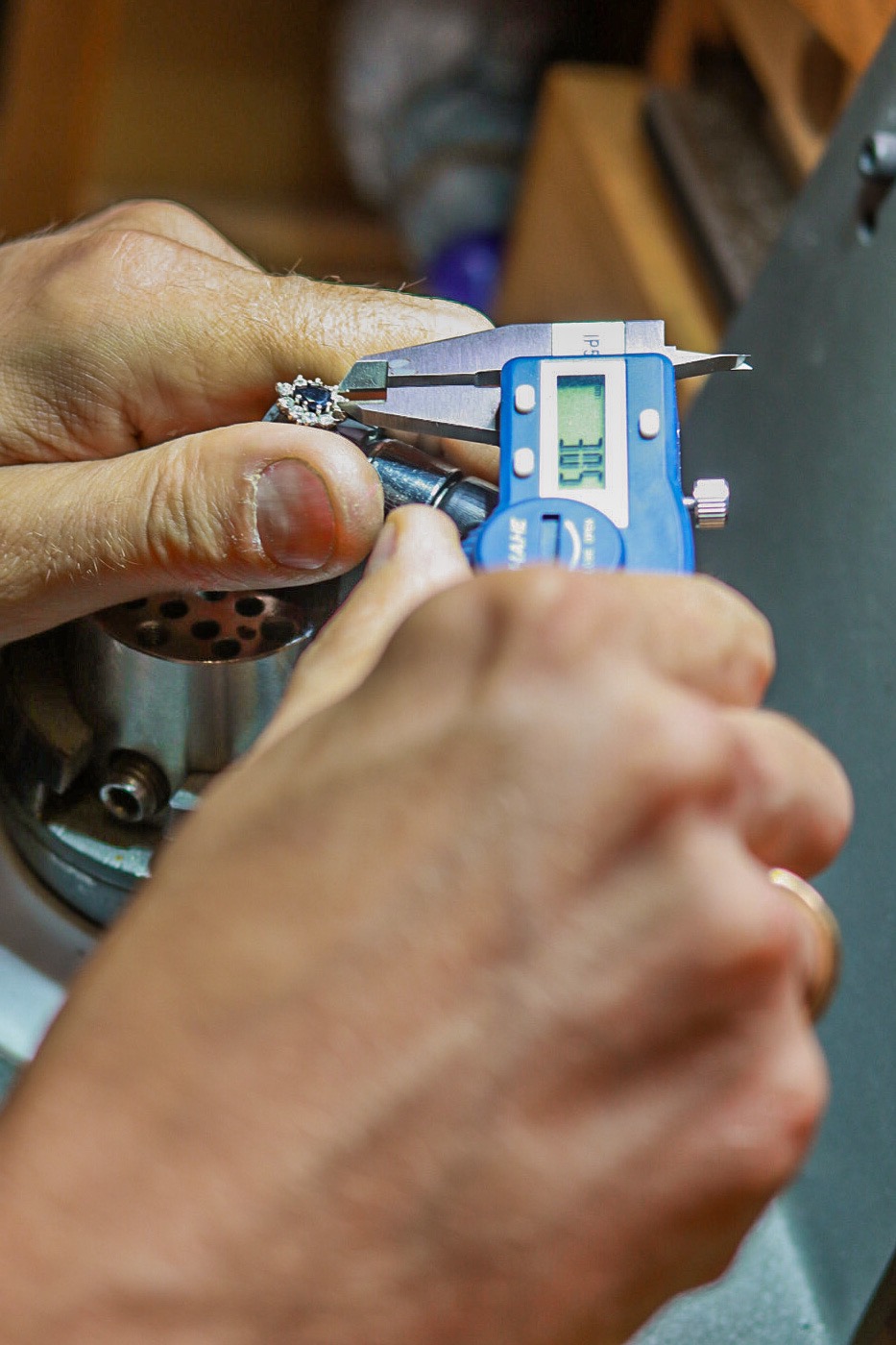 Jubiler mierzy średnicę oczka pierścionka z szafirem i diamentami za pomocą cyfrowego suwmiarki.