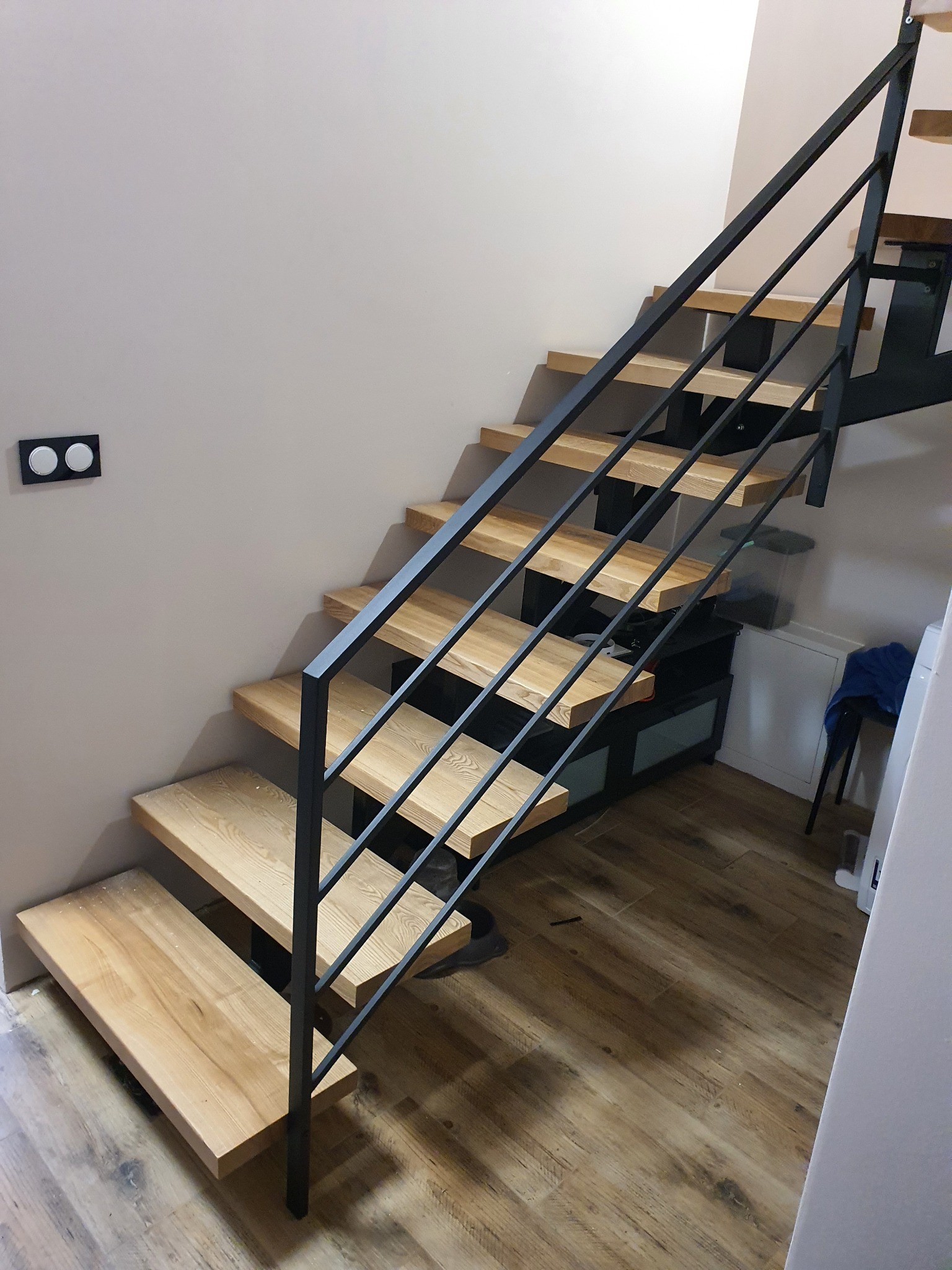 Schody drewniane z czarną metalową balustradą w nowoczesnym wnętrzu, widok z dołu, oświetlenie naturalne.