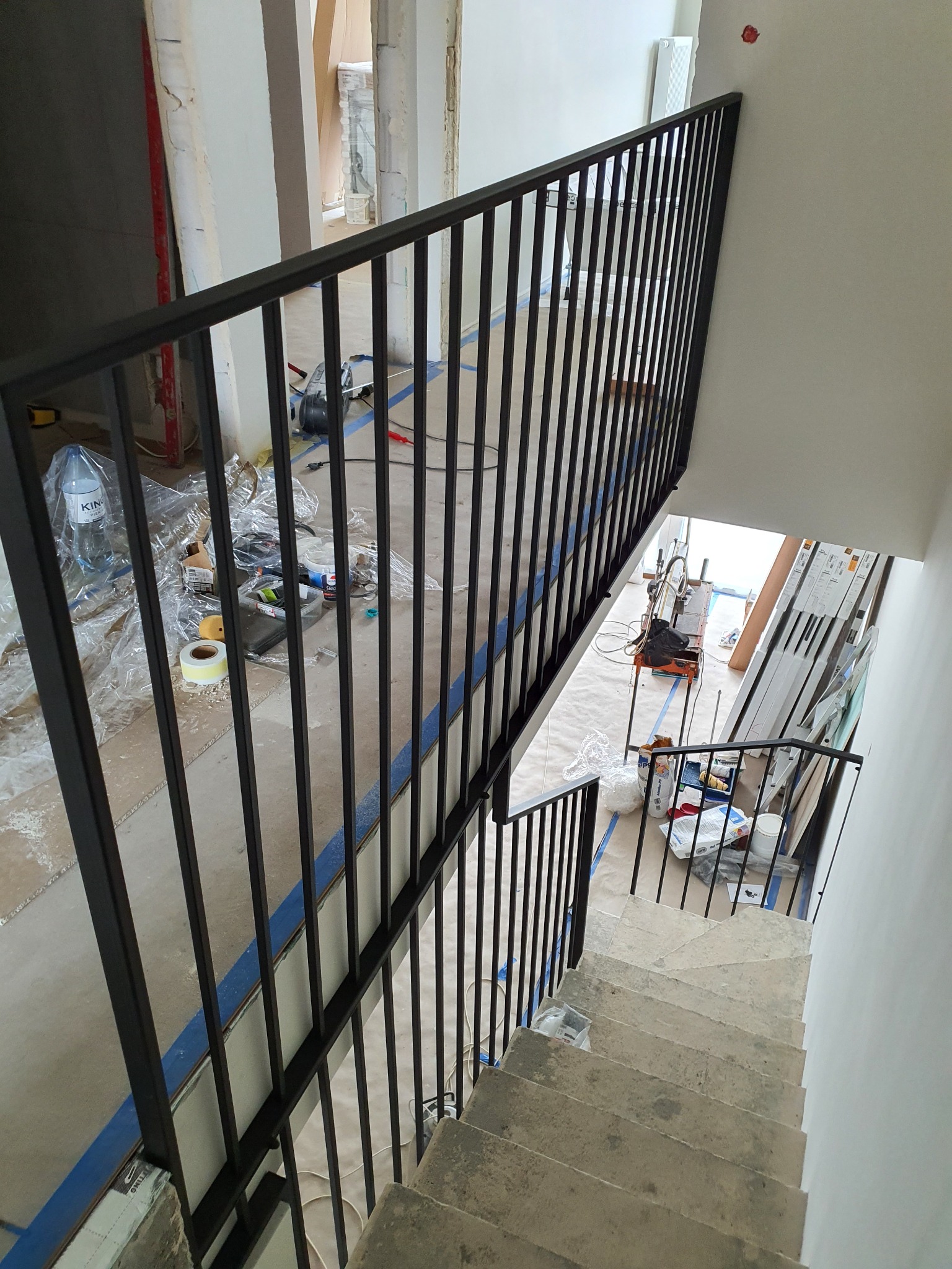 Nowoczesna czarna balustrada schodowa z pionowych prętów, widok z góry na surowe schody i zaplecze z narzędziami i materiałami budowlanymi.