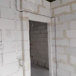 Surowy stan: kable elektryczne prowadzone po ścianach z bloczków w nowym budynku, przed tynkowaniem. Widoczne uchwyty mocujące przewody.