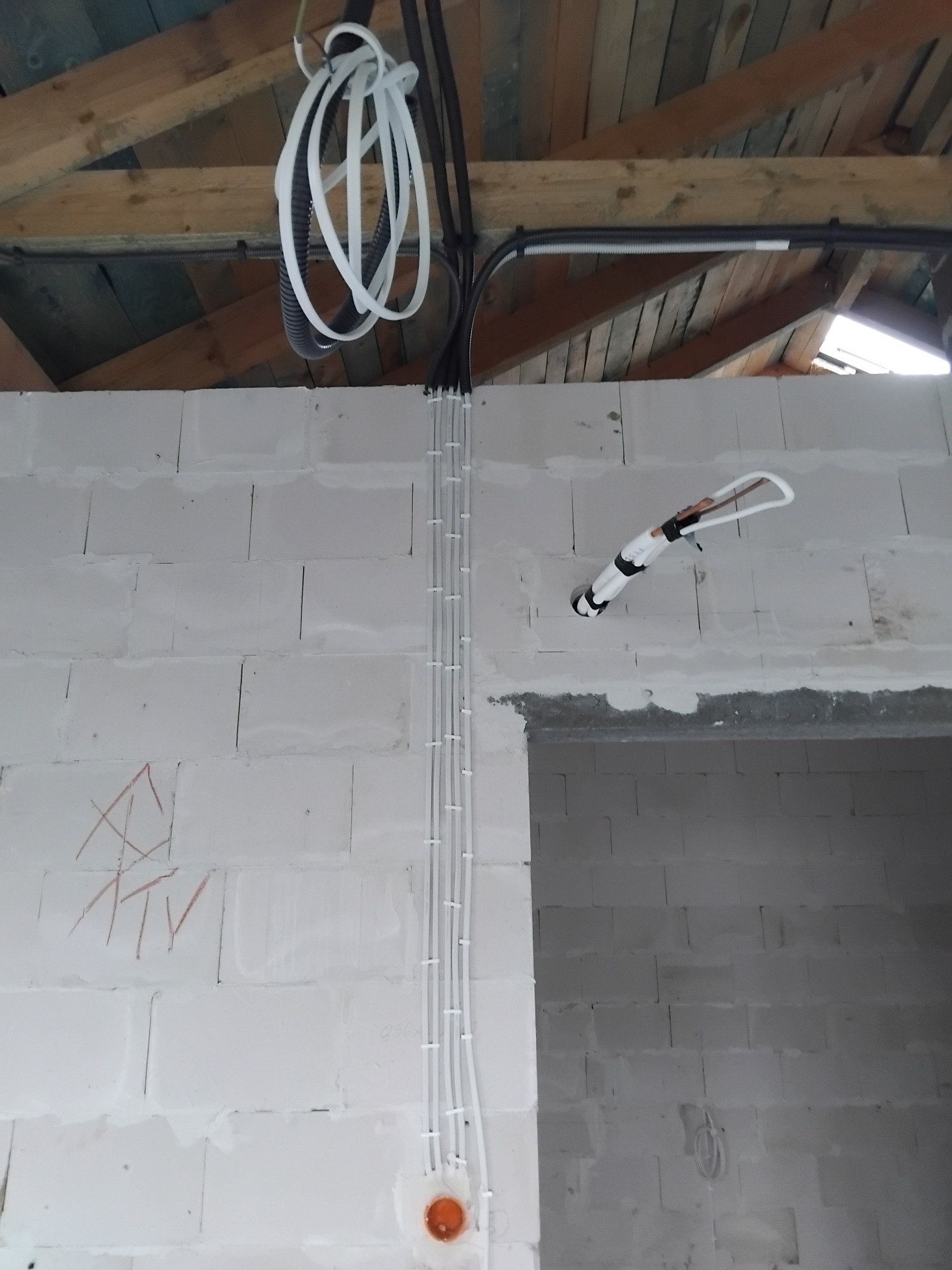 Białe kable elektryczne prowadzone pionowo po ścianie z bloczków, mocowane opaskami. Widoczne także kable pod sufitem z drewnianych belek.