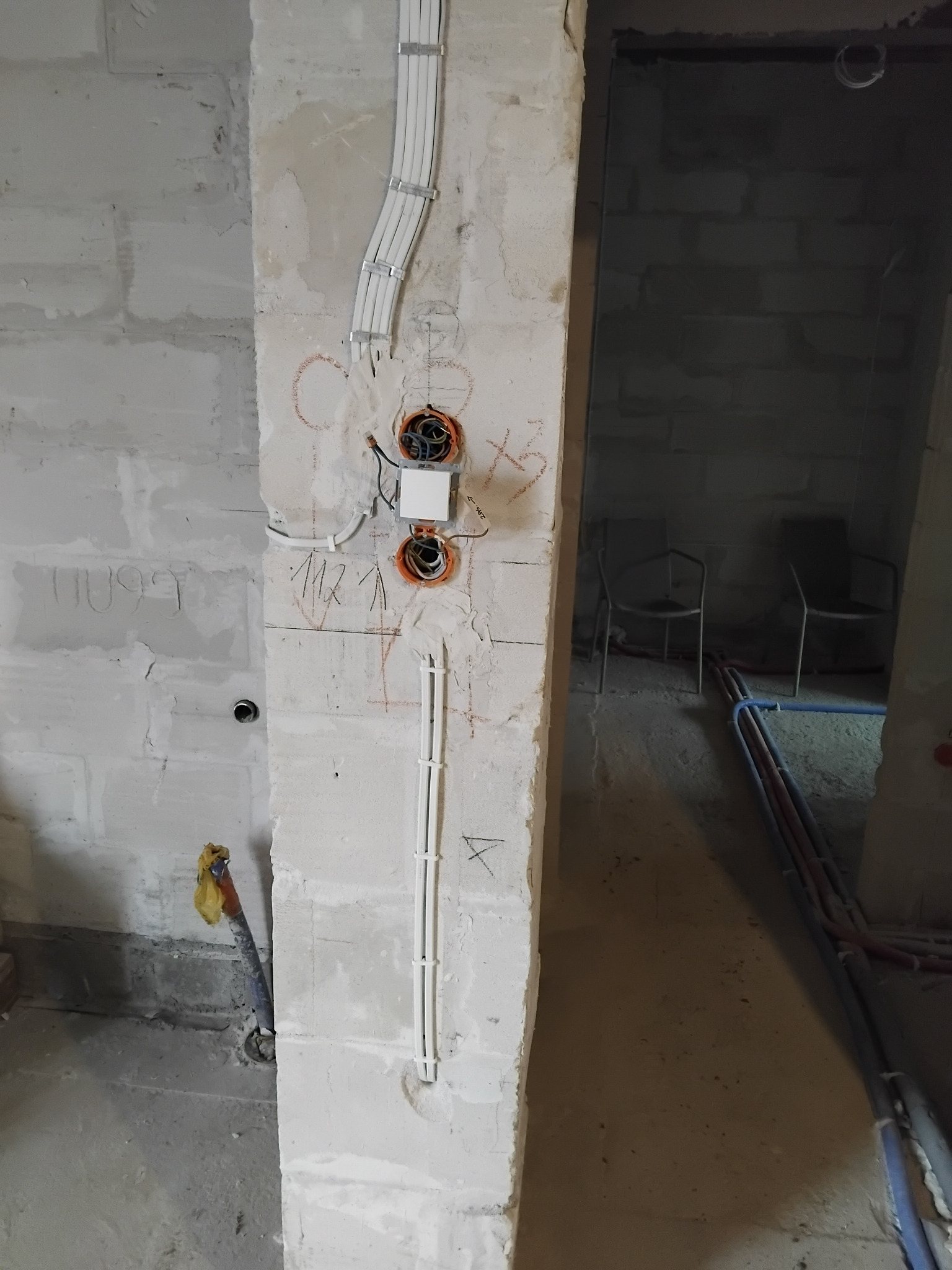 Wewnętrzna instalacja elektryczna w surowym budynku, widoczne kable w peszlach, puszki instalacyjne i fragment włącznika na ścianie z betonu komórkowego.