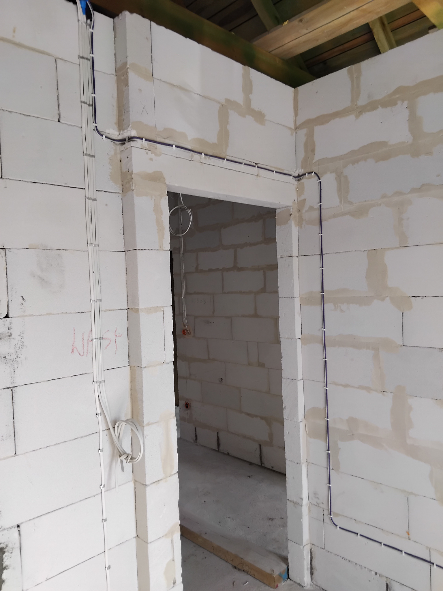 Surowy stan: kable elektryczne prowadzone po ścianach z bloczków w nowym budynku, przed tynkowaniem. Widoczne uchwyty mocujące przewody.