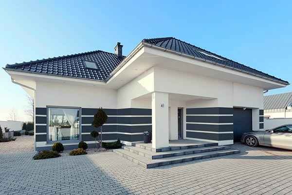 Nowoczesny dom jednorodzinny z białymi ścianami i grafitowymi akcentami, widok z zewnątrz na elewację z oknem i wejściem, kostka brukowa na podjeździe.