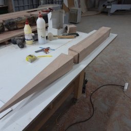 Wood-Pol - Drewniany element o kształcie strzały, przygotowywany do montażu, leży na stole warsztatowym obok narzędzi i kleju.