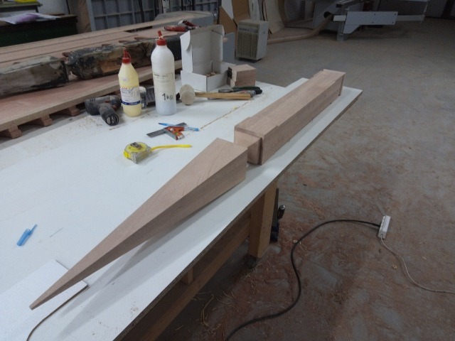 Drewniany element o kształcie strzały, przygotowywany do montażu, leży na stole warsztatowym obok narzędzi i kleju.