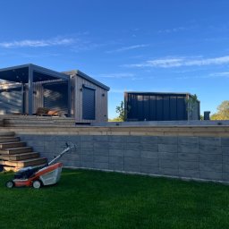 SADZIMYTO - Grzegorz Malinowski - Nowoczesny ogród z pergolą, drewnianymi schodami i równo skoszoną trawą. W tle widoczny budynek. Na pierwszym planie kosiarka do trawy.