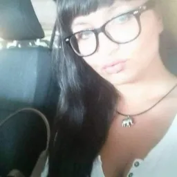 Kobieta w okularach i z wisiorkiem słonia robi selfie w samochodzie, widoczny zagłówek fotela.