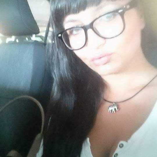 Kobieta w okularach i z wisiorkiem słonia robi selfie w samochodzie, widoczny zagłówek fotela.