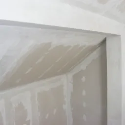 Niedokończone połączenie płyty kartonowo-gipsowej z sufitem w rogu pokoju, widoczne ślady szpachlowania i łączenia.