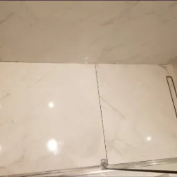 Białe, marmurowe płytki podłogowe w kabinie prysznicowej z odpływem liniowym, widok z góry.