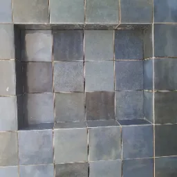 Niebiesko-szare kwadratowe płytki z wnęką w ścianie, widoczne drewniane elementy konstrukcyjne u dołu.