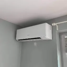 Biały klimatyzator marki Fuji Electric zamontowany na szarej ścianie w pokoju, widoczne ślady po wcześniejszym montażu na ścianie.