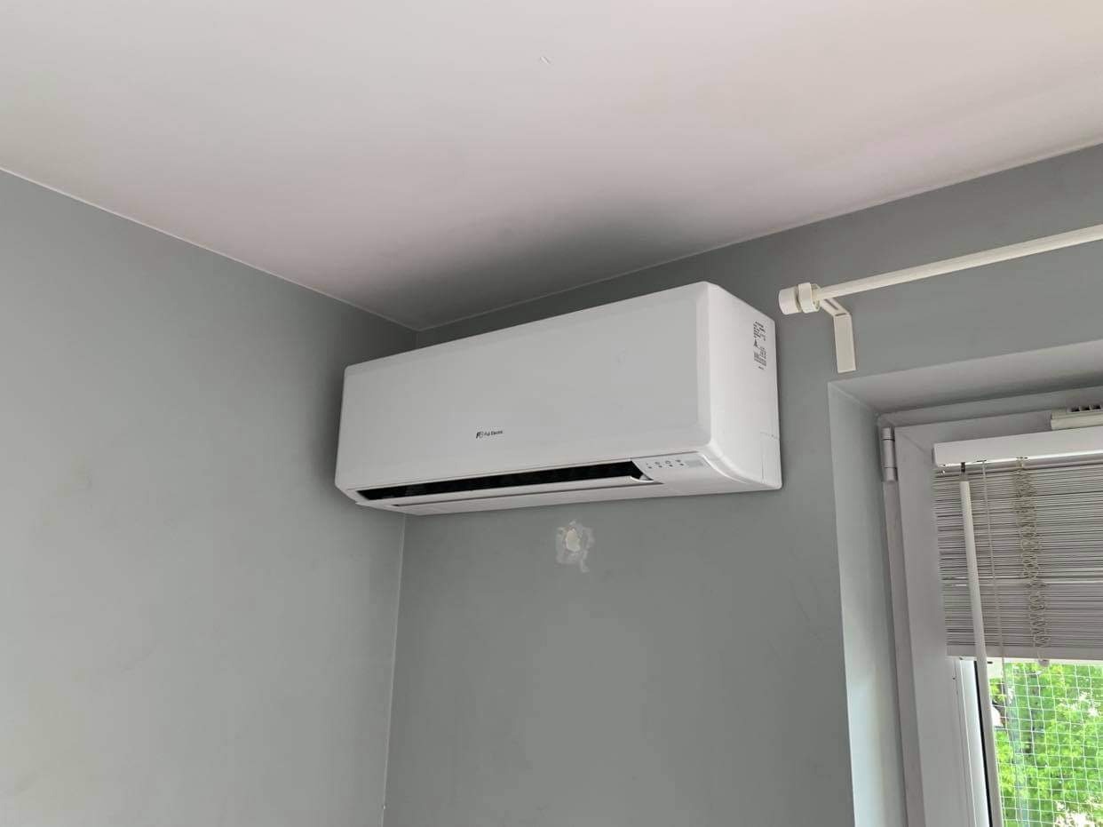 Biały klimatyzator marki Fuji Electric zamontowany na szarej ścianie w pokoju, widoczne ślady po wcześniejszym montażu na ścianie.