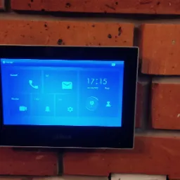 Panel wideodomofonu Dahua zamontowany na ceglanej ścianie, wyświetlający menu główne z ikonami połączeń, wiadomości, monitoringu i ustawień.