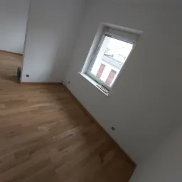 Jasny parkiet ułożony w nowym pokoju z białymi ścianami i oknem z widokiem na budynki.