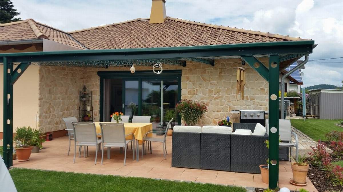 Zadaszony taras z kamienną elewacją, meblami ogrodowymi i grillem, wykończony zieloną konstrukcją nośną.