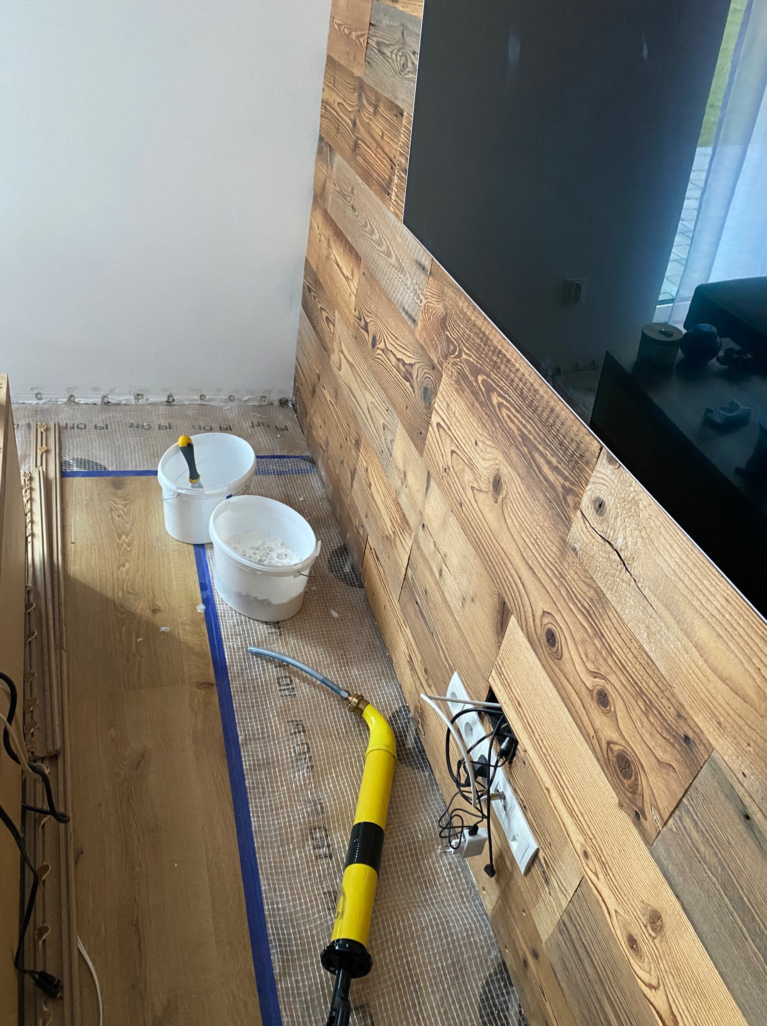 Montaż drewnianej okładziny ściennej z widocznymi puszkami elektrycznymi i narzędziami. Prace wykończeniowe w trakcie realizacji.