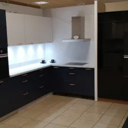 Nowoczesna kuchnia z granatowymi szafkami, białymi górnymi szafkami, marmurowym blatem i miedzianymi uchwytami, z czarnymi urządzeniami AGD marki Layman.