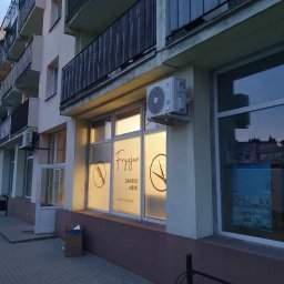 MG-Klima TABAKA Marek Giemza - Zewnętrzny klimatyzator zamontowany nad oknem lokalu usługowego z napisem 'Fryzjer damsko-męski Anna Przemyska', grafiki grzebienia i nożyczek na oknie, widok z chodnika.