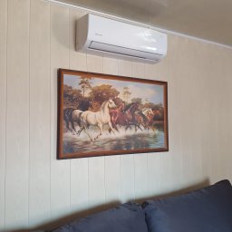MG-Klima TABAKA Marek Giemza - Biały klimatyzator marki Rotenso zamontowany nad obrazem z motywem koni, na ścianie wyłożonej panelami.