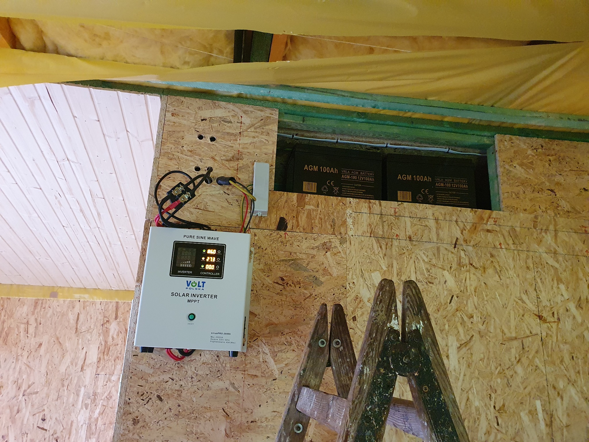 Instalacja fotowoltaiczna wyspowa w drewnianej konstrukcji: falownik Volt Polska, dwa akumulatory AGM 100Ah i drabina oparta o ścianę z płyty OSB.
