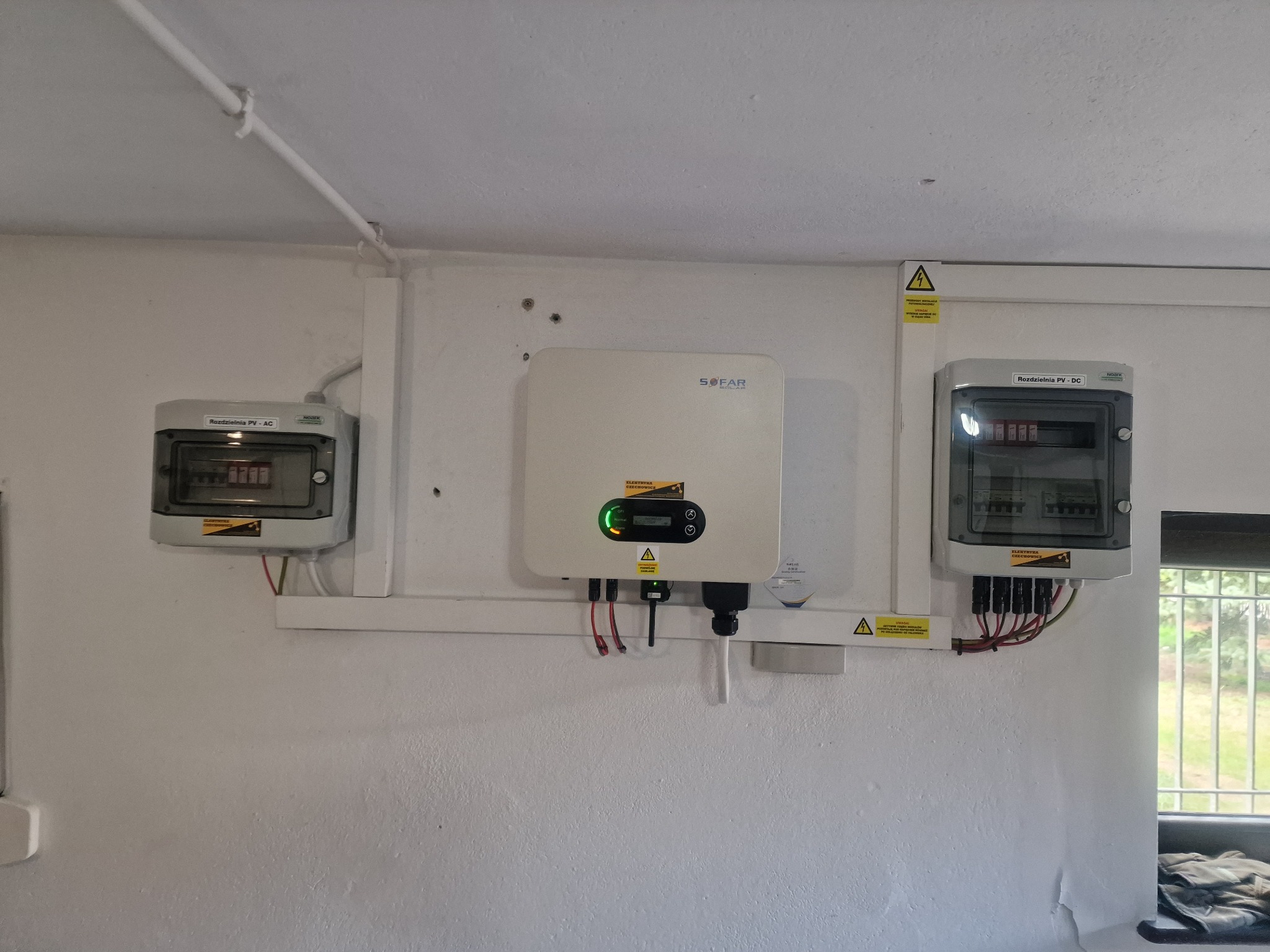 Zamontowany inwerter SOFAR z dwoma rozdzielnicami PV-DC na białej ścianie, widoczne okablowanie i naklejki ostrzegawcze.