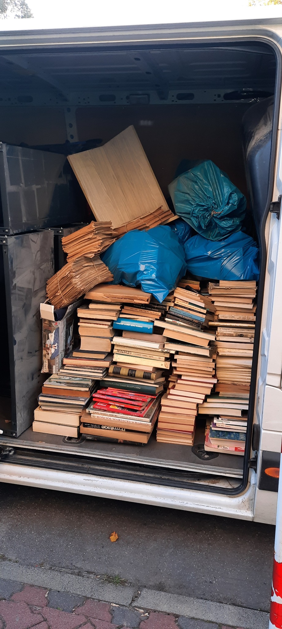 Wnętrze busa wypełnione książkami, dokumentami i workami podczas przeprowadzki w Gołaszynie. Część przedmiotów zabezpieczona folią.