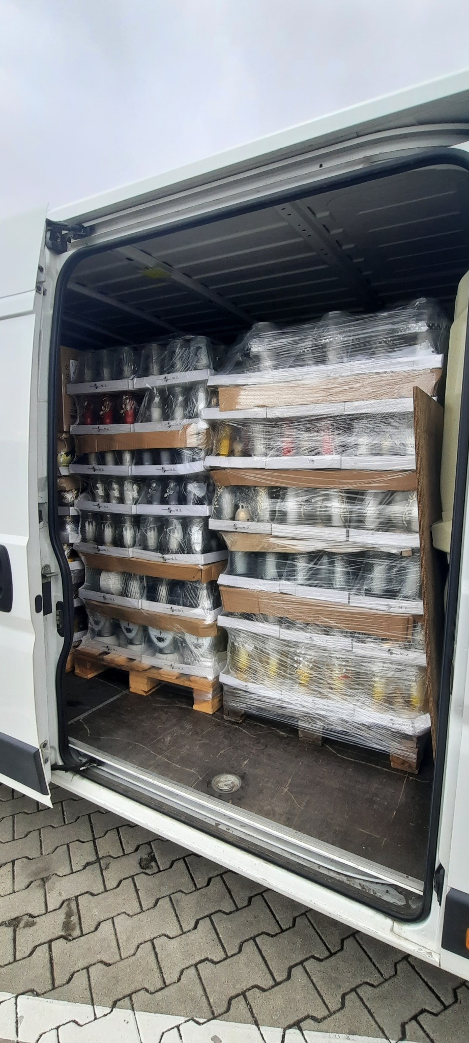 Wnętrze białego busa wypełnione paletami z zapakowanymi zniczami, zabezpieczonymi folią stretch.