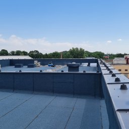 Daad Matter Spółka z Ograniczoną Odpowiedzialnością - Widok z góry na płaski dach pokryty papą termozgrzewalną z widocznymi elementami mocującymi, w tle zabudowania przemysłowe i zieleń.