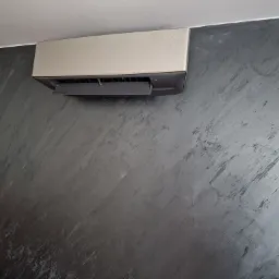 Zamontowana jednostka wewnętrzna klimatyzatora na ścianie z dekoracyjnym efektem betonu architektonicznego, widok z dołu.