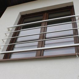 SPEED balustradydlaciebie.pl - Okna zabezpieczone poziomymi, metalowymi prętami ochronnymi z kwadratowymi zakończeniami, zamontowane na elewacji domu z brązową ramą okienną i systemem alarmowym.