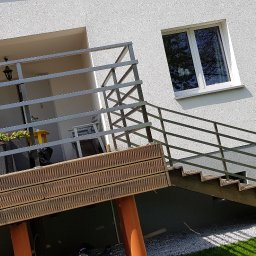 SPEED balustradydlaciebie.pl - Zewnętrzne schody z drewnianymi stopniami i metalową, poziomą balustradą, prowadzące na taras z widocznymi donicami, na tle białego budynku z oknami.
