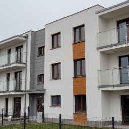 SPEED balustradydlaciebie.pl - Nowoczesny budynek wielorodzinny z balkonami zabezpieczonymi balustradami szklanymi i elementami ze stali nierdzewnej, widok z poziomu gruntu.