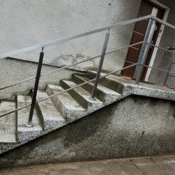 SPEED balustradydlaciebie.pl - Zewnętrzne schody z szarego lastryko z prostą balustradą ze stali nierdzewnej, widok z dołu na tle elewacji budynku i pojemników na śmieci.