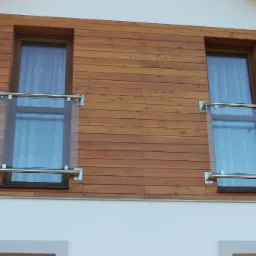 Dwa okna z zamontowanymi zewnętrznymi balustradami szklanymi z elementami ze stali nierdzewnej, umieszczone na elewacji wykończonej drewnianą boazerią.